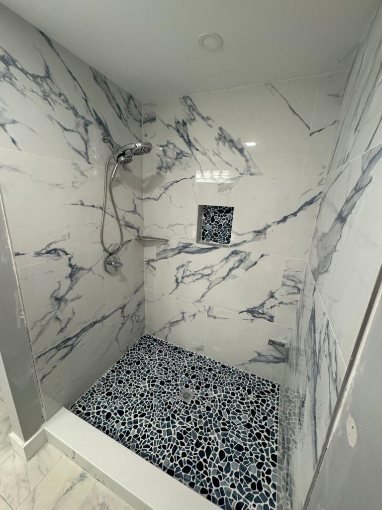 Completed white marble-look walk-in shower with black pebble floor by Luxe Revamp