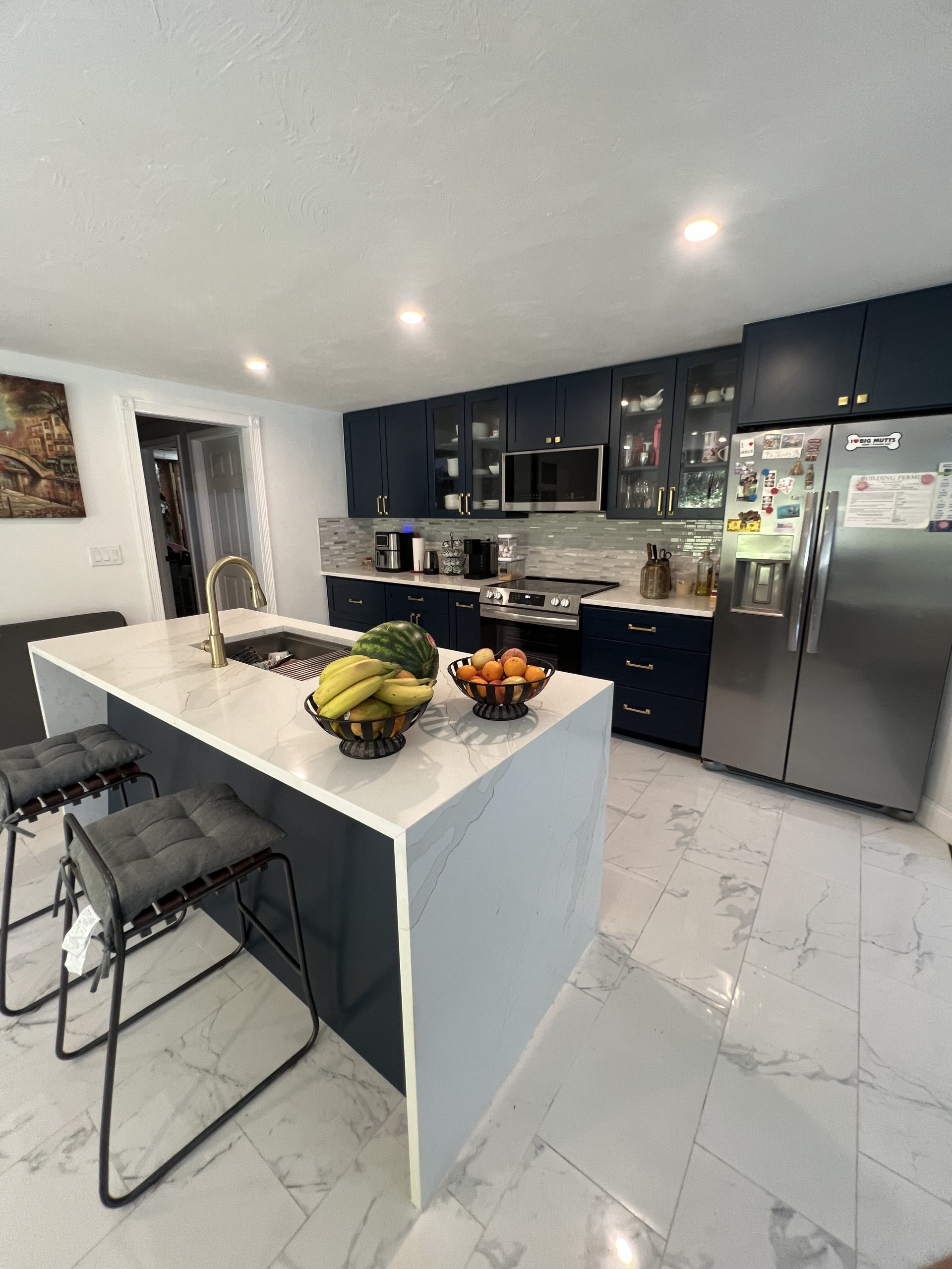 Renovated kitchen with waterfall island, navy cabinetry and white marble-look tile floor by Luxe Revamp